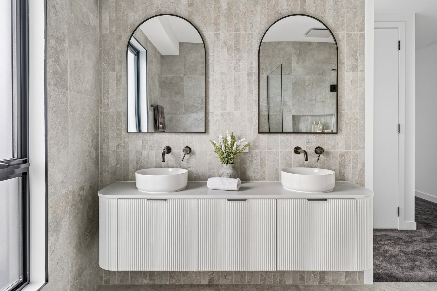 Bathroom with a double vanity, arched mirrors, grey tiles and freestanding bath at Kostas Street, Sunbury.