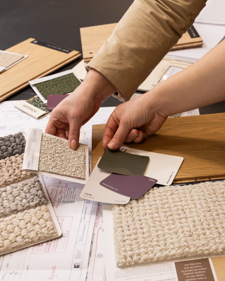 Hands comparing carpet, paint and material samples over project plans for the TimTek showroom