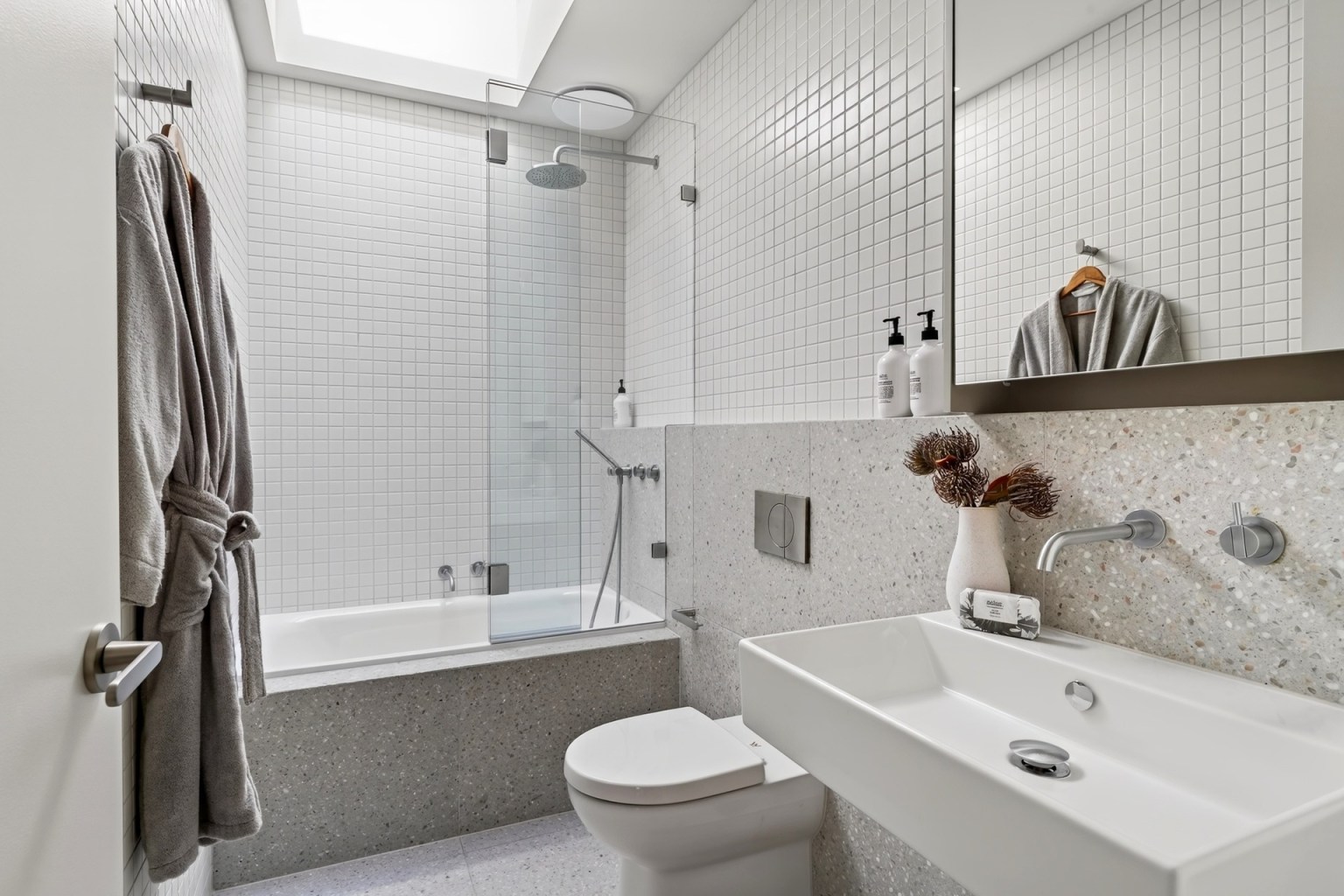 Skylit white-tiled bathroom with bath, shower, basin and terrazzo surfaces at Carrigal Street, Balwyn.
