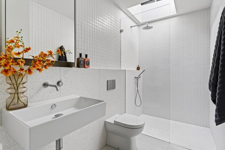 White tiled bathroom with skylight and orange flowers at 1 Carrigal Street