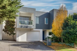 Contemporary grey and white home exterior framed by autumn landscaping in Kew