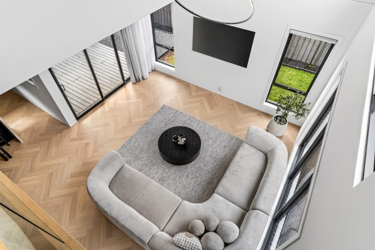 Double-height living room with a curved sofa and herringbone timber floor in Sunbury