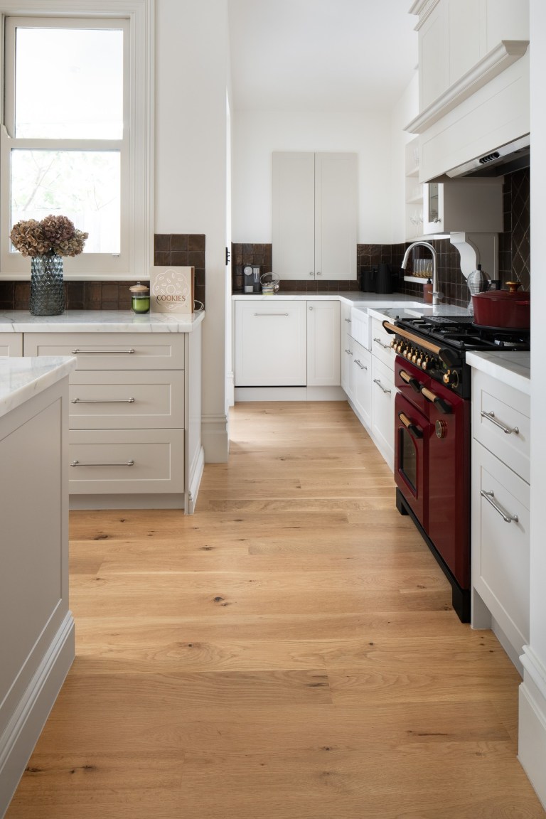 White galley kitchen with timber flooring and a red range in Prahran